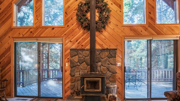 Un interior de madera con chimenea de piedra, ventanas grandes y una terraza.
