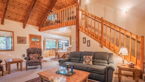 Amplia sala de estar con escalera de madera, un sofá cómodo, un comedor y vistas al exterior.