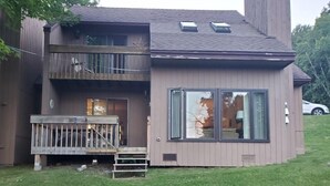 A two-story house with a balcony, large windows, and a fire pit in the yard. - Bright mountain condo w/ fireplace near Sugarbush (Warren)