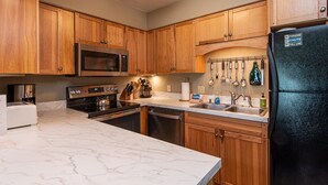 A kitchen with wooden cabinets, a black refrigerator, a microwave, a stove, and a sink. - Bright mountain condo w/ fireplace near Sugarbush (Warren)