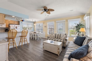 A spacious living area with a dining table, two wooden chairs, a striped sofa, a coffee table, and a ceiling fan.