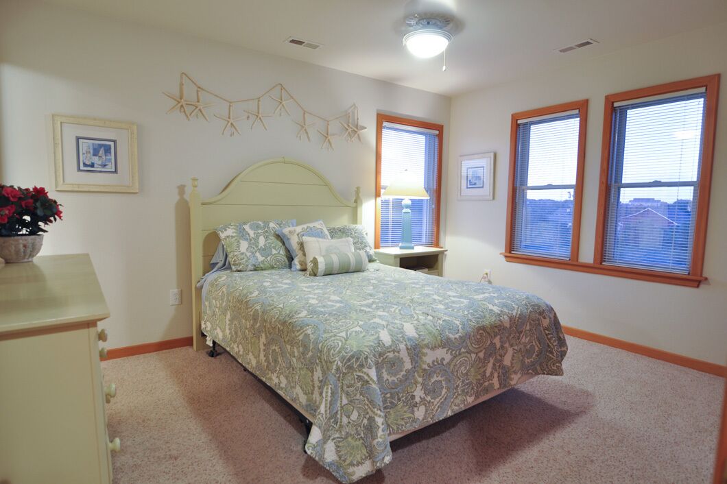 A bedroom with a bed, a nightstand, a dresser, and a window with blinds.