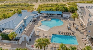 An aerial view of a resort with a large central pool, multiple smaller pools, and outdoor seating areas.