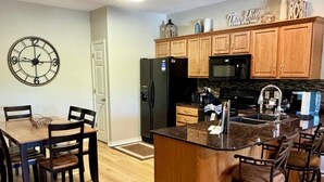 A modern kitchen with wooden cabinets, a black refrigerator, a microwave, and a large island with bar stools. - 3 BR 2 Bath Vickery Resort Walk In Condo, on Table Rock Lake with Dock Access (Hollister)