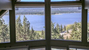 Vista de dentro de um edifício com grandes janelas, com vista para um lago rodeado de árvores.