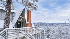 Um edifício coberto de neve com uma escadaria que leva a um deck com vista para um lago e montanhas.