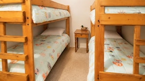 A room with two bunk beds, a small wooden nightstand, and a ceiling light.