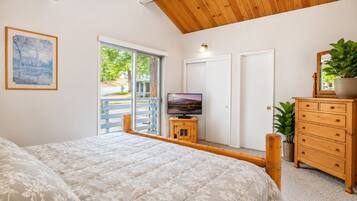A bedroom with a bed, a TV, a wooden dresser, and a door leading to an outdoor area.