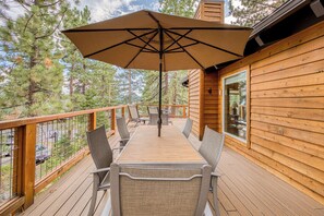 Una terraza de madera con una mesa, sillas y una sombrilla, con vistas a árboles.