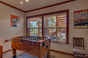 A room with a foosball table, a window with a view of trees, and a poster on the wall.