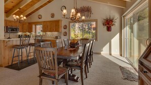 A spacious kitchen with wooden beams, a dining area with a large table and chairs, and a view through a sliding glass door.