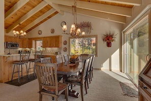 A spacious kitchen with wooden beams, a dining area with a large table and chairs, and a view through a sliding glass door.