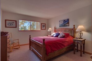 Un dormitorio con una cama de madera, dos mesitas de noche con lámparas, un sillón mecedora y cuadros enmarcados en las paredes.
