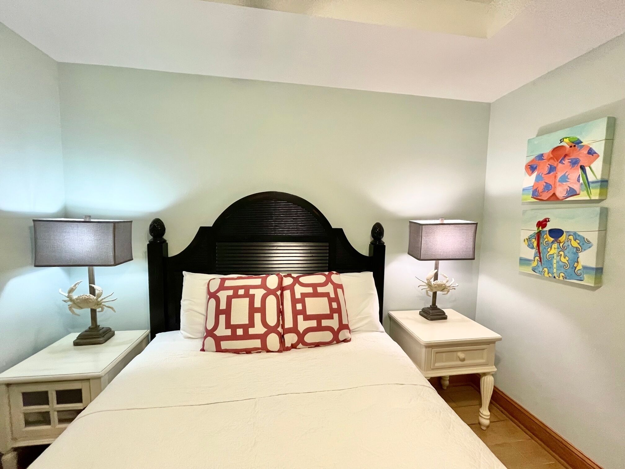 A neatly made bed with a patterned pillow, two bedside lamps, and a nightstand with a decorative crab.