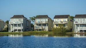 A row of waterfront houses with balconies, a lake in the foreground, and a clear sky. - Outer Banks Bliss: 3-bedroom Cottage in Golf Community, Beach Club Access (Nags Head)