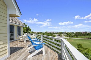 A wooden deck with blue chairs and a white fence overlooking a green landscape.