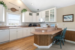 Une cuisine moderne avec des meubles blancs, un îlot central en bois et une vue sur l’extérieur.