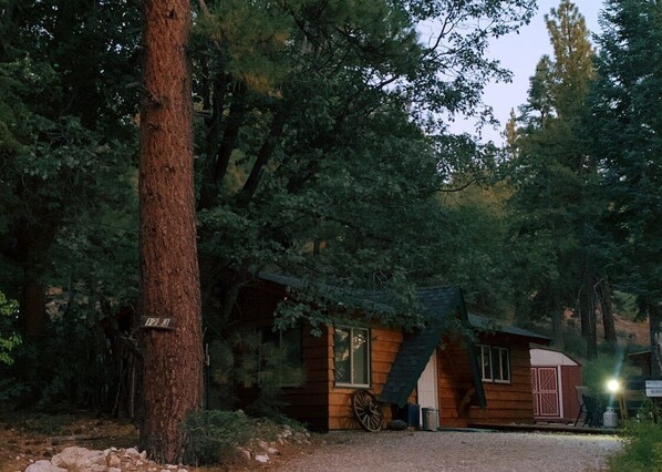 A rustic cabin with a wooden exterior, a wheelbarrow, and a sign indicating the number 12.6.