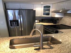 A kitchen with a stainless steel refrigerator, a microwave, a stove, and a sink with a modern faucet.