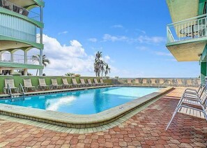 A swimming pool with lounge chairs, a clear sky, and a building with balconies.