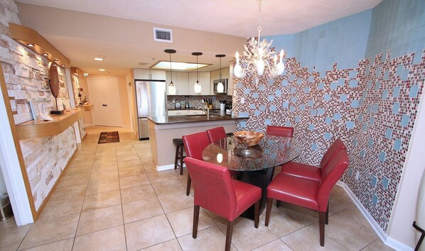 A modern kitchen with a central island, red chairs, and a mosaic wall.
