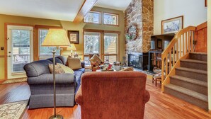 A cozy living room with a fireplace, a staircase, and a large window.