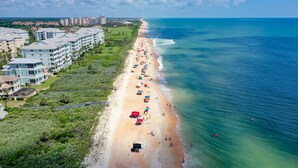 An aerial view of a beach with multiple buildings, a sandy shore, and a clear blue ocean. - Cinnamon Beach Unit 323- Just a few steps to the Sun and Sand! (Palm Coast)