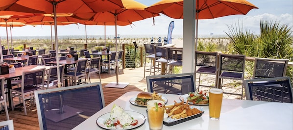 Un espace de restauration en plein air avec des tables, des chaises, des parasols et une vue sur la plage.