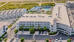 Un hotel costero con varias edificaciones, un estacionamiento y una playa al fondo.