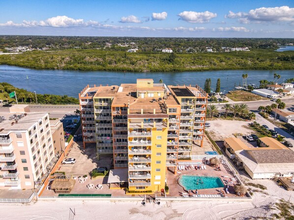 Ein mehrgeschossiges Hotel mit Balkonen, einem Schwimmbad und Blick auf Wasser und Grünflächen.