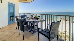 A balcony with a table set for dining, overlooking a beach. - Beach Palms 507 -Gulf front luxurious Condo - Spectacular Views! (Indian Shores)