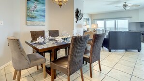 A dining area with a chandelier, wicker chairs, and a painting on the wall. - Beach Palms 507 -Gulf front luxurious Condo - Spectacular Views! (Indian Shores)