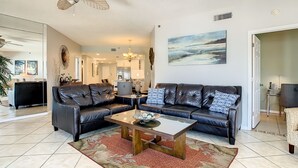 A spacious living room with two black leather sofas, a wooden coffee table, and a large painting on the wall. - Beach Palms 507 -Gulf front luxurious Condo - Spectacular Views! (Indian Shores)
