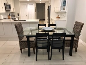 Une cuisine moderne avec des meubles blancs, un réfrigérateur en acier inoxydable et une table à manger en verre, accompagnée de quatre chaises.