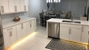 Una cocina moderna con armarios blancos, lavavajillas de acero inoxidable y un comedor con mesa y sillas de vidrio.
