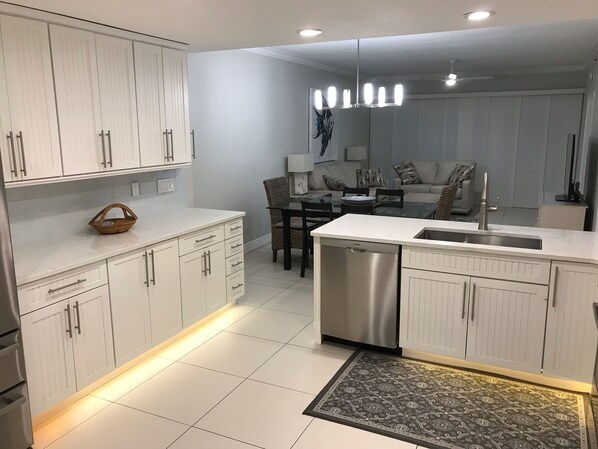 Una cocina moderna con armarios blancos, lavavajillas de acero inoxidable y un comedor con mesa y sillas de vidrio.