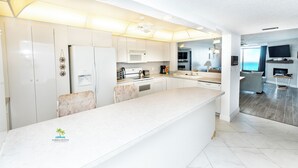 A modern kitchen with white cabinetry, a large island, and a dining area with a view of the ocean. - Quiet Waters Condominium 5B (Indian Shores)