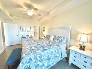 A bedroom with a bed, a nightstand, a bench, a ceiling fan, and a door.
