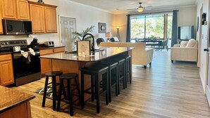 Een moderne keuken met houten kastjes, een centraal eiland met krukken, en een zithoek met een bank en tafel.