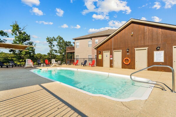 A swimming pool with lounge chairs and a lifebuoy, surrounded by a building with a wooden exterior and a covered area.