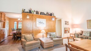 Una sala de estar acogedora con techo de madera, un comedor con mesa y sillas, y una cocina con armarios de madera.