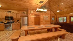 A wooden cabin interior with a kitchen, dining table, benches, and a ceiling fan. - Live, Laugh, Love Pool Lodge: Indoor Pool, Theater (Cosby)