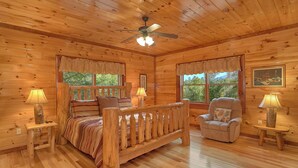 A cozy cabin room with a wooden bed, a chair, and a desk with lamps. - Live, Laugh, Love Pool Lodge: Indoor Pool, Theater (Cosby)