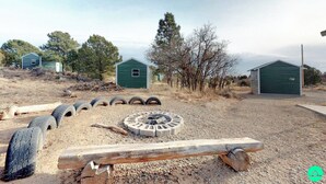 A rustic outdoor setting with a fire pit, wooden benches, and green sheds in a dry, gravelly area with sparse vegetation. - W-W: Pavilion and Glamping Village (Monticello)