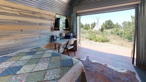 A bedroom with a large bed, a desk, and a chair. There is a window with a view of the outdoors.