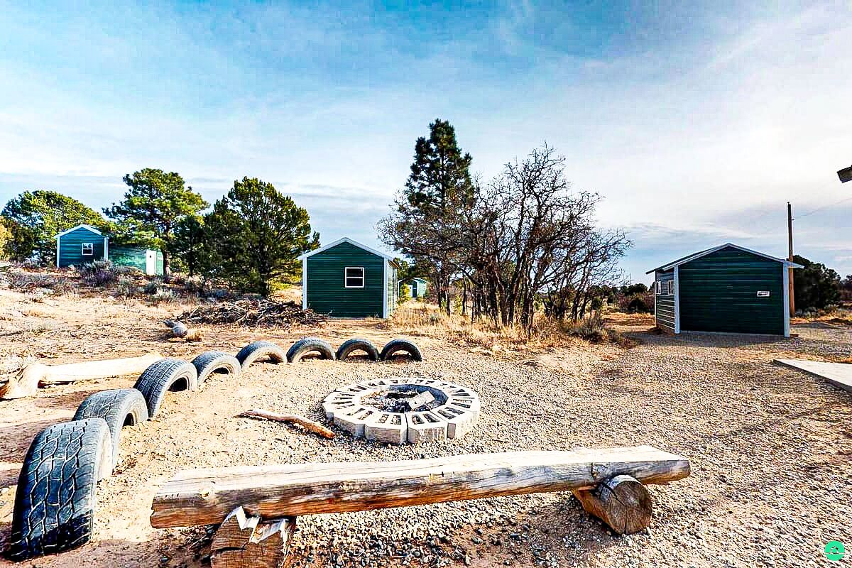 A rural setting with two green sheds, a fire pit, and scattered tires.