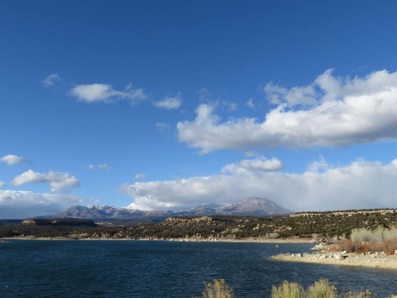 A coastal landscape with a mountain range in the background, a clear sky, and a body of water in the foreground.
