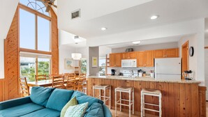 Una cocina moderna con armarios de madera, una isla central con taburetes y un comedor con mobiliario de madera.