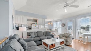 A modern living room with a grey sectional sofa, a white coffee table, and a ceiling fan. - Southern Reach: Soundside Golf Villa w/ Beach Club Access and Sunset Views (Nags Head)