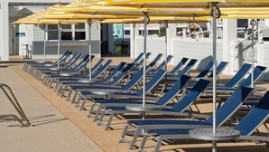 Eine Reihe von Liegestühlen mit gestreiften Sonnenschirmen, ein Poolbereich und ein Gebäude mit geneigtem Dach im Hintergrund.